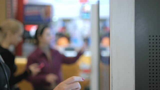 Girl using touch terminal makes a quick order through the self-service. Woman choosing dessert via self-service machine at fast food restaurant. Person swipes the screen making an order.