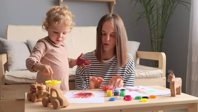 Creative family collaboration. Artistic partnership. Parental creativity. Kid-friendly art. Pretty happy smiling mother with her little baby daughter painting together in home interior.