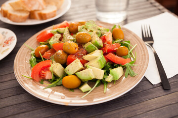 fresh salad of arugula, avocado, cherry tomatoes with olives on brown plate