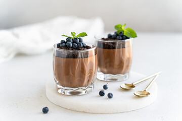 Healthy vegan chocolate mousse with fresh blueberry and mint in glasses on white background....