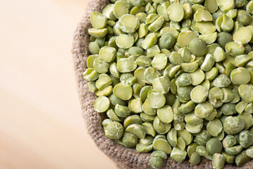 Close up of dry green pea beans in small bag with wooden background. Dehydrated green pea in linen sack