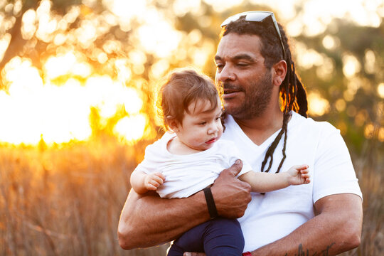 Aboriginal man with baby daughter in country setting at sunset