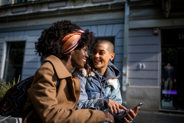 Happy young mixed lesbian couple using a smartphone together while walking in the city