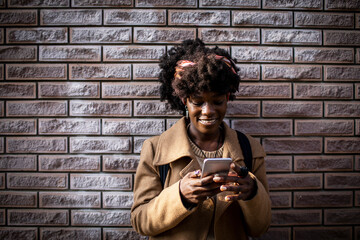 Portrait of a young African American woman using a smartphone with a brick wall background