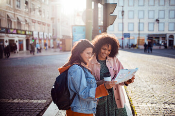 Two diverse female friends using a map to navigate the city on vacation