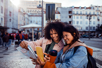 Two diverse female friends using a map to navigate the city on vacation