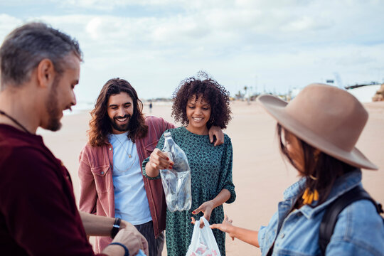 Trio of diverse friends recycling plastic waste from a beach - Powered by Adobe