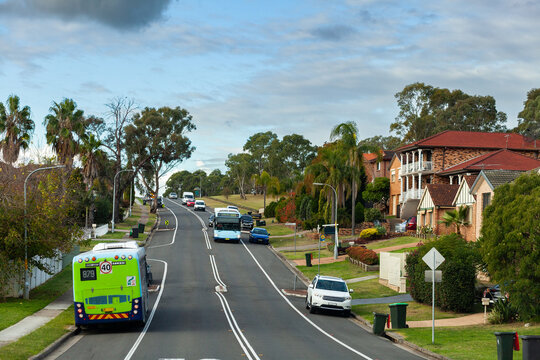 Green bus pulling over to the side of the road and blue bus driving down street