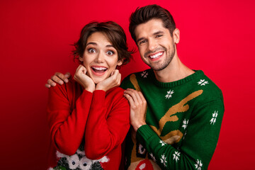 Photo of dreamy excited married couple wear ornament sweaters arms cheeks cuddling isolated red color background