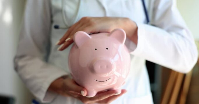 Nurse doctor woman with stethoscope holding pink piggy bank. Health insurance health care and medicine