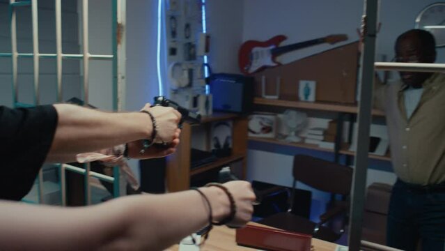 POV shot of two young Caucasian robbers pointing guns at black male pawnbroker giving items they want at pawnshop