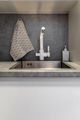 Sink part of a shot in a luxurious kitchen. Gray marble countertop and white crane.