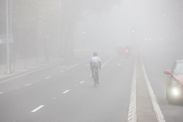 Cyclist riding down city road in mist