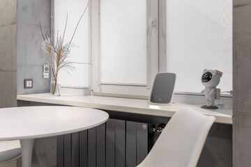 Round white table standing near the window, on the windowsill dry plants in a vase