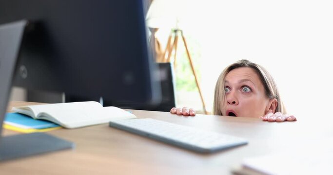 Woman in shock and surprise looks from under table at computer. Emotions of fear of surprise and on Internet
