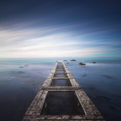 Fototapeta premium Wooden pier remains in a blue sea. Long Exposure.
