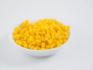 A  bowl full of natural yellow beeswax peals isolated on a white background