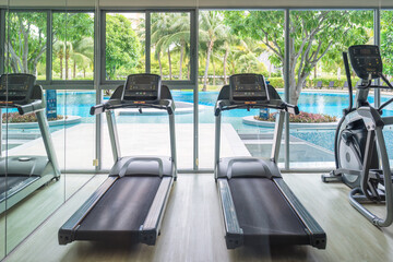 Fototapeta premium Row of treadmill machine and glass window with garden view in gym