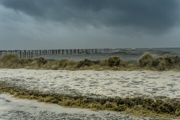 Rough see with violent waves with a broken pier on the background. Harsh storm condition with muddy...
