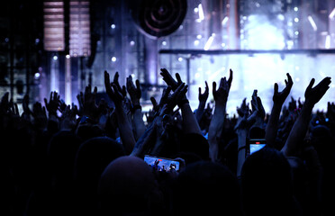 Fototapeta na wymiar Performance of a popular group. The crowd with raised hands against the stage light