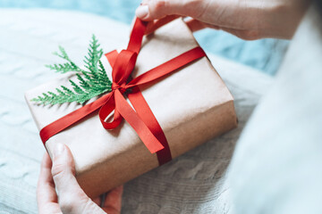 Female hands holding gift handcrafted box thoughtfully wrapped in eco-friendly packaging with with red ribbon bow. Sustainable and eco conscious living concept.