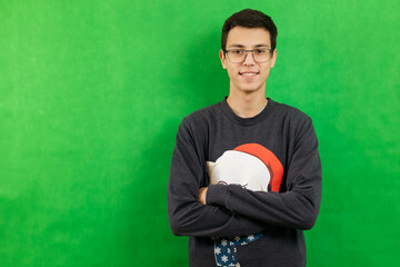 Portrait of a young man in glasses and Christmas clothes on a green background, looking at the camera, smiling. Chroma key, copy space