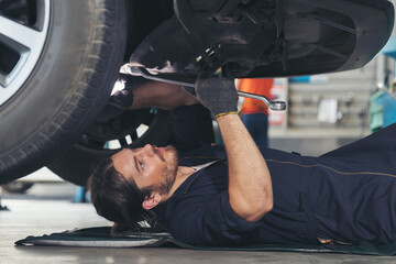 Male car mechanic worker working and repair, maintenance underneath lifted car. Mechanic vehicle...