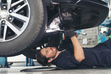 Male car mechanic worker working and repair, maintenance underneath lifted car. Mechanic vehicle...