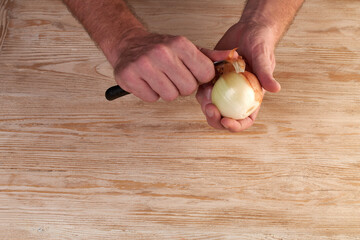 Men's hands are peels fresh onion with knife