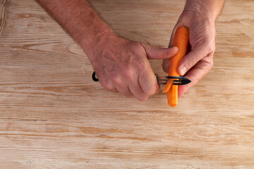Men's hands are peels fresh carrots with a vegetable cutter