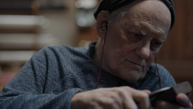 Senior gray haired male master in a wheelchair working at his workshop sharpening japanese deba knife