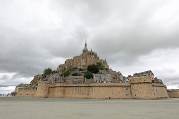 ancient Mont Saint Michel abbey and the protective walls of the hill during low tide with the beach