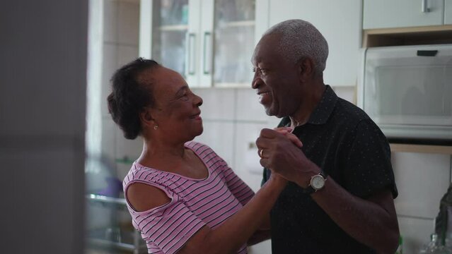 A happy Brazilian black couple engaged in candid dance at home kitchen, romantic authentic moment between elderly Senior man and woman