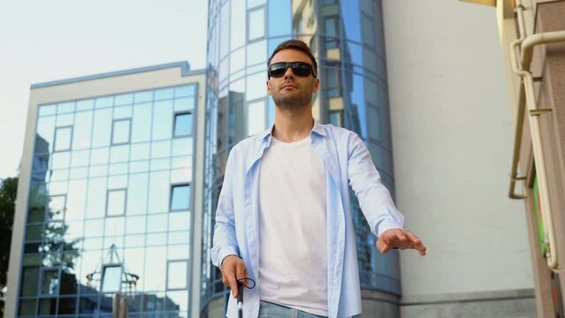 A blind man walks on the street. Visually impaired man with walking stick