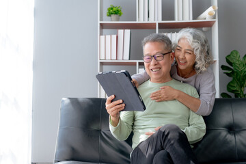 Happy mature couple using tablet at home. Happy elderly Asian couple laughing bonding together sitting at home table with tablet.