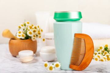 Shampoo and hair comb with chamomile. Hair cosmetics with chamomile extract. Chamomile flowers and cosmetic tubes of shampoo and essential oil on a textured wooden background. Flatley. Copy space.