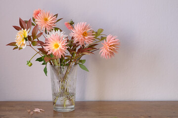 Autumn bouquet of salmon-colored dahlias and peony leaves in a glass vase on the table