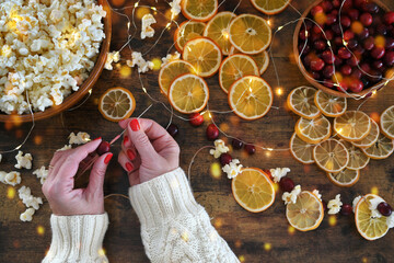 Woman making Christmas garland by stringing popcorn, cranberries, dried orange and lemon slices © MargJohnsonVA