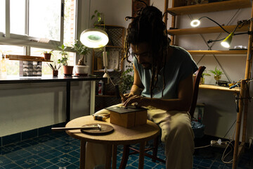 Goldsmith hammering a piece in a home jewelry workshop. Young Rastafarian