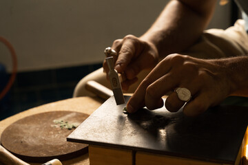 Goldsmith's hands hammering jewelry stone on a wooden plate in a goldsmith's workshop. Natural...