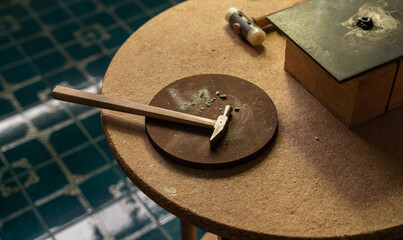 Hammer and circular metal plate on a table in a goldsmith's workshop.