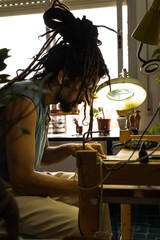 Young Rastafarian artisan jeweler working in his home workshop. Vertical photo. Concentrated at work.