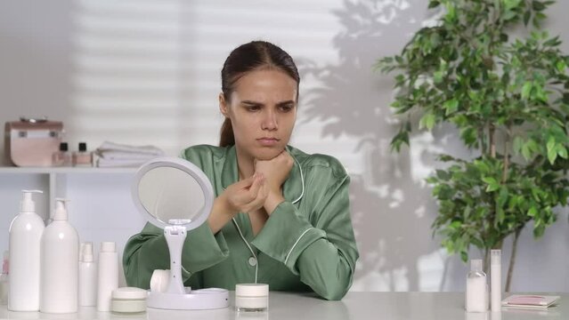 A young woman runs her hand over her face, left unsatisfied with the oiliness of her skin. A woman applies lotion or micellar water to a cotton pad and wipes her face.