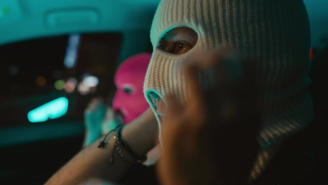 Close up side handheld shot of young caucasian couple putting on balaclavas, taking guns, fooling and kissing in car before robbery