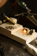 Vertical photo of a burning torch heating a piece of jewelry in a goldsmith's workshop.