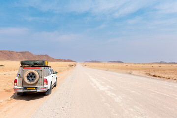 Pickup truck driving on long straight desert road towards mountains. - obrazy, fototapety, plakaty
