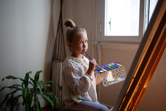 little cute girl draws with paints on canvas at the easel