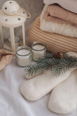 Cozy home interior. Knitted sweaters, mittens, candles and Christmas decor. Cozy winter concept.