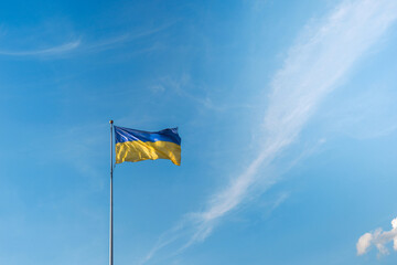 Flag of Ukraine on flagstock over blue sky