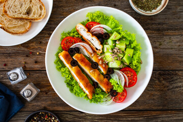 Caesar style salad - fried breaded chicken breast and vegetables on wooden table
